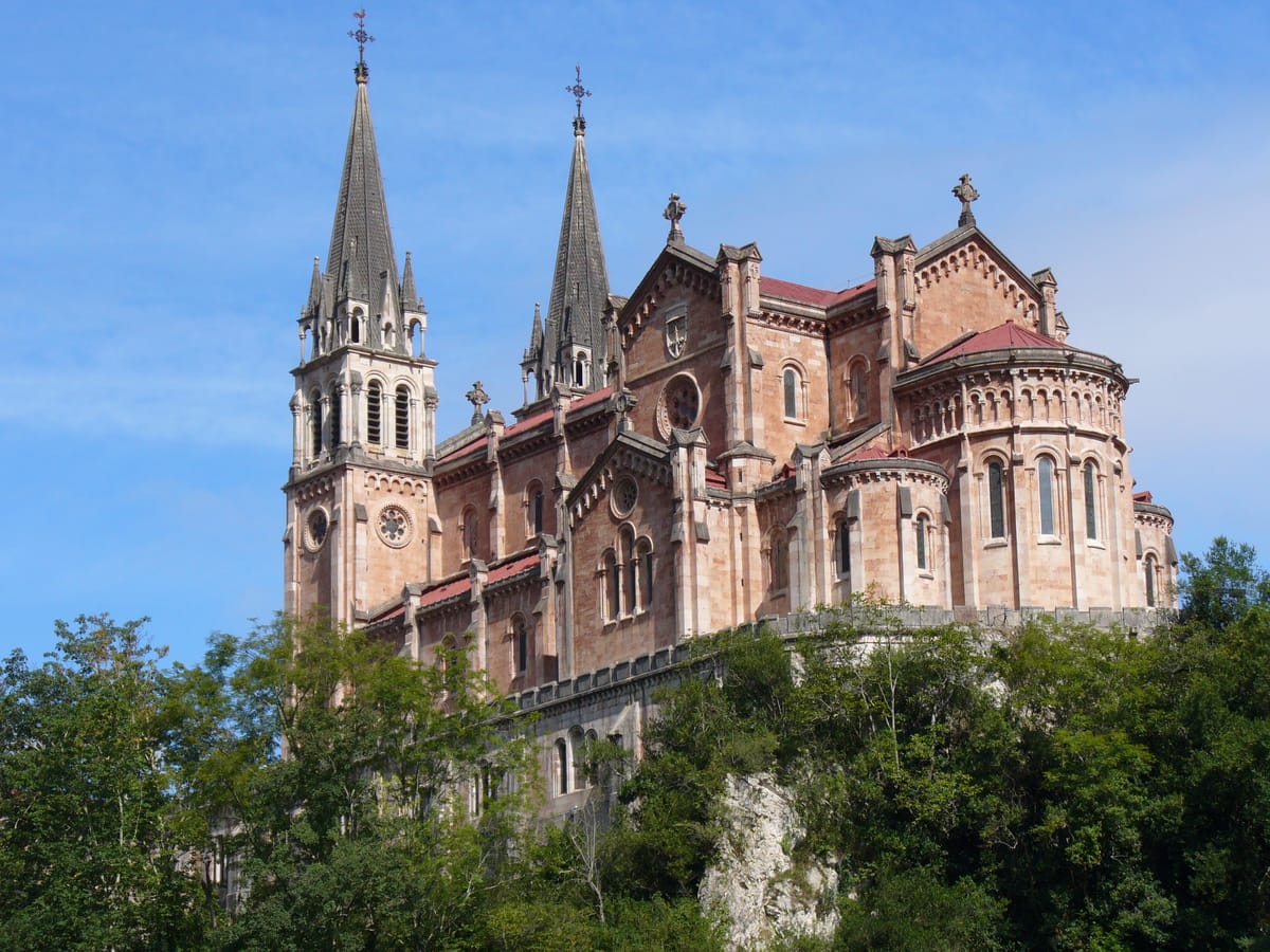 Basílica de pedra rosada com duas torres de agulha, vista de baixo, entre árvores