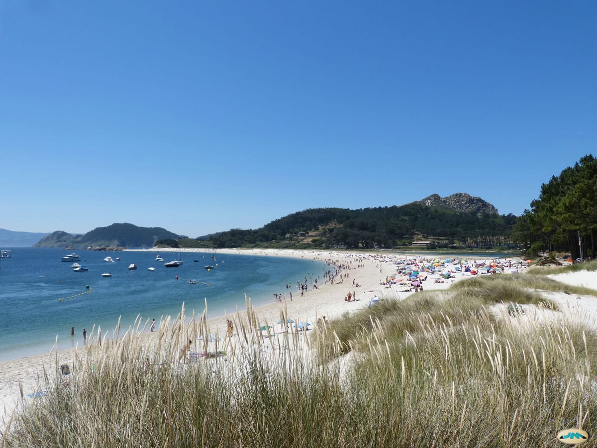 Praia de areia clara em arco, com água transparente e mata ao fundo, nas ilhas Cíes