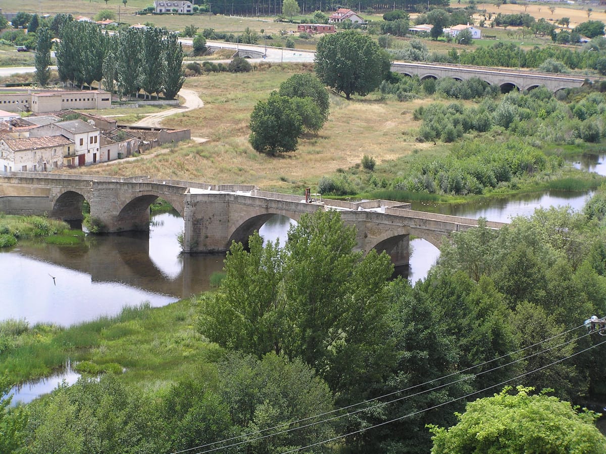 Ponte de pedra de vários arcos sobre o rio Águeda, com vegetação nas margens