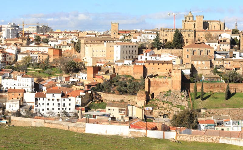 Vista da Ciudad Monumental de Cáceres ao entardecer, com as torres medievais de pedra douradas pela luz do sol