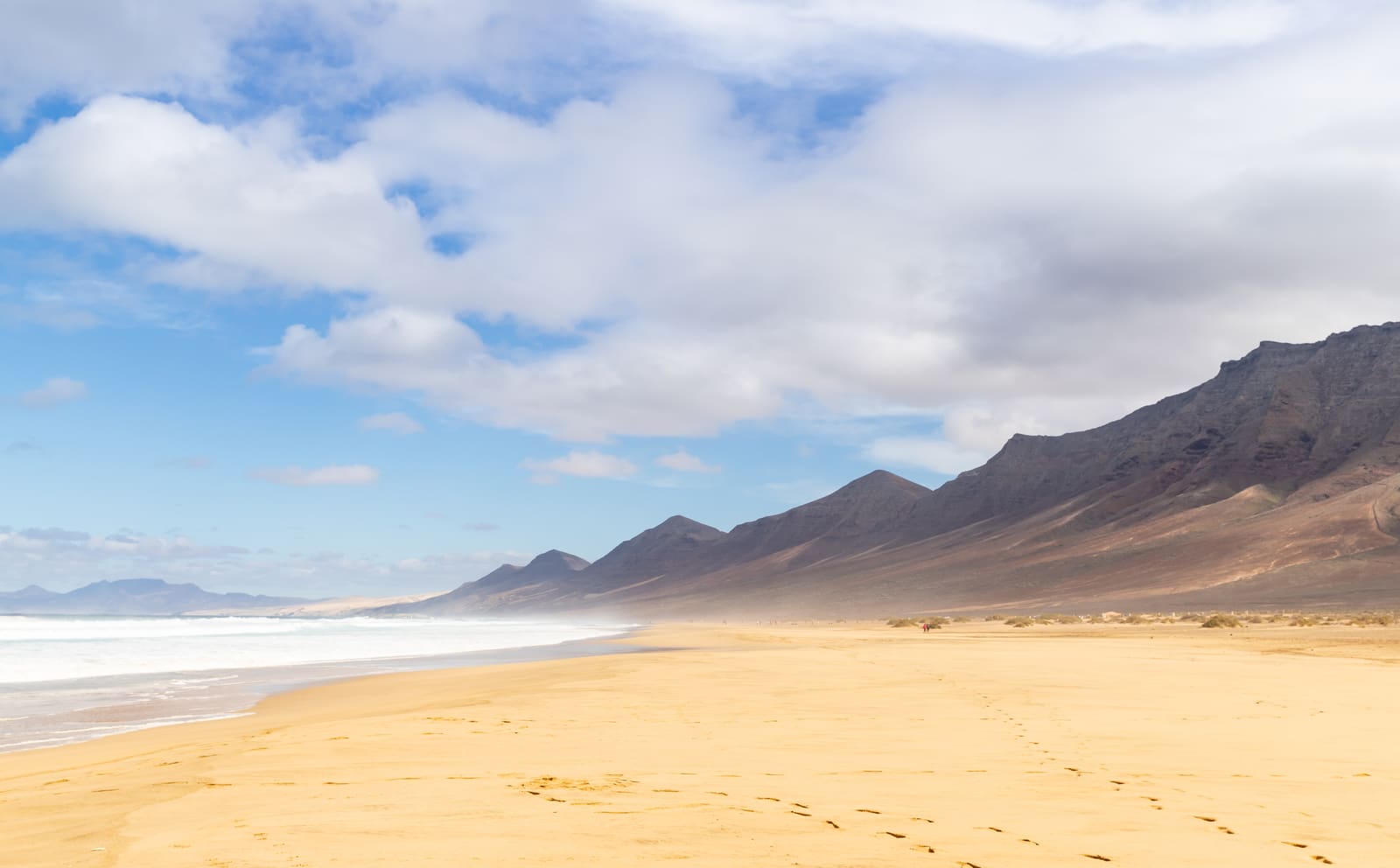 Praia de Cofete, em Fuerteventura, com areia dourada e montanhas sob nuvens