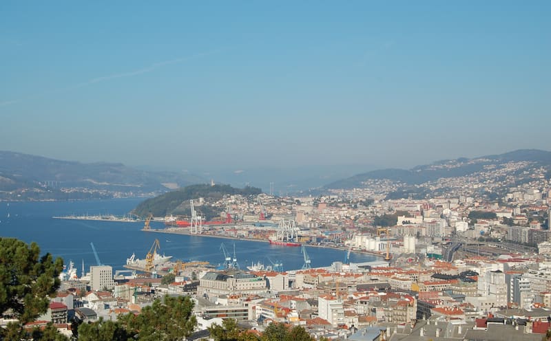 Vista do centro de Vigo e do porto, com guindastes à beira da ria e morros ao fundo
