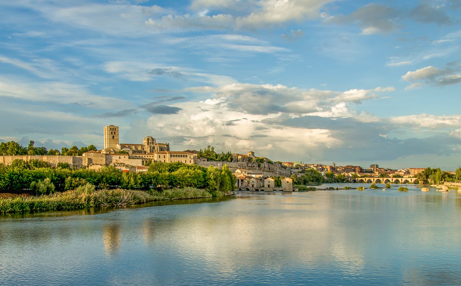 A catedral de Zamora no alto da muralha, refletida no rio Douro, com as aceñas e a ponte de pedra ao fundo